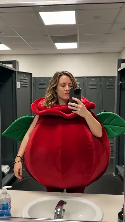 AI Halloween Costume example: a woman in a giant red rose costume takes a mirror selfie in a gym locker room