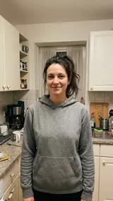 The photo used for this example: a smiling woman with a messy dark ponytail in a grey hoodie stands by kitchen cabinets