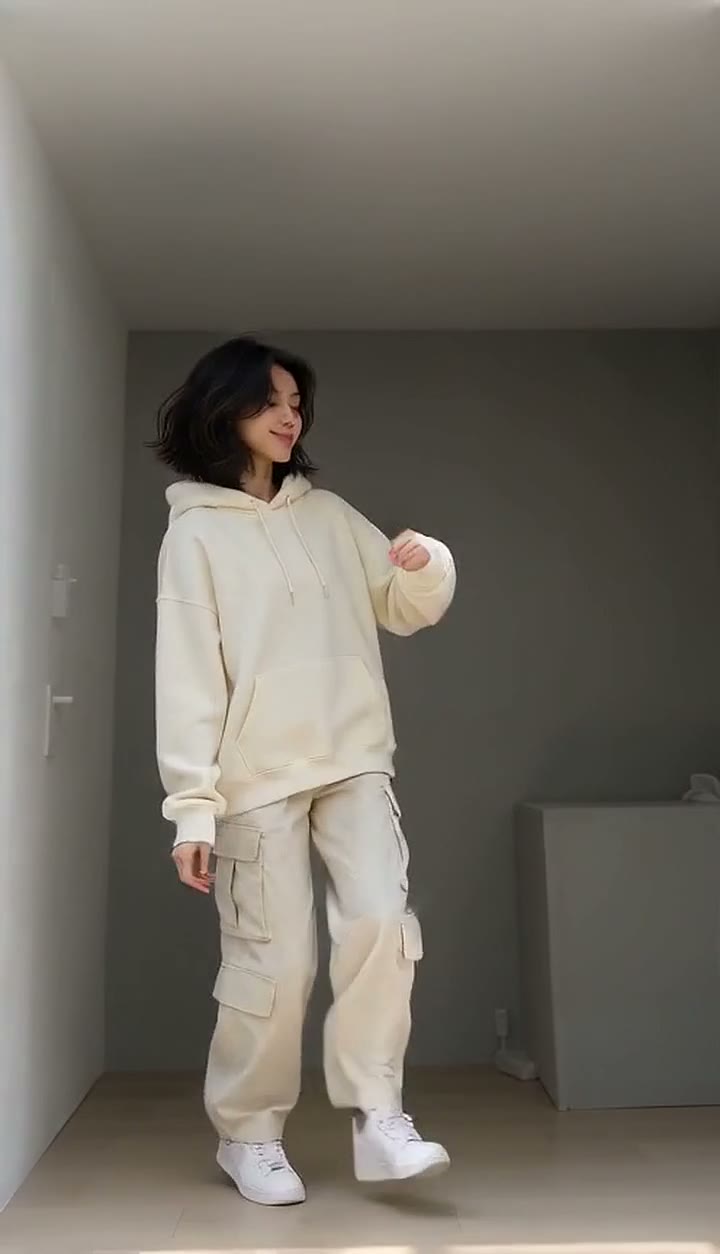 Toc Toc AI Dance example: a woman in a cream hoodie and cargo pants dances in a small grey room