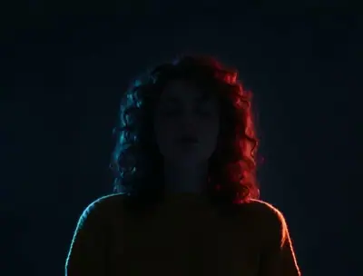 Turn The Lights Off AI example: a woman with curly hair stands with closed eyes in a dark room lit by red and blue light